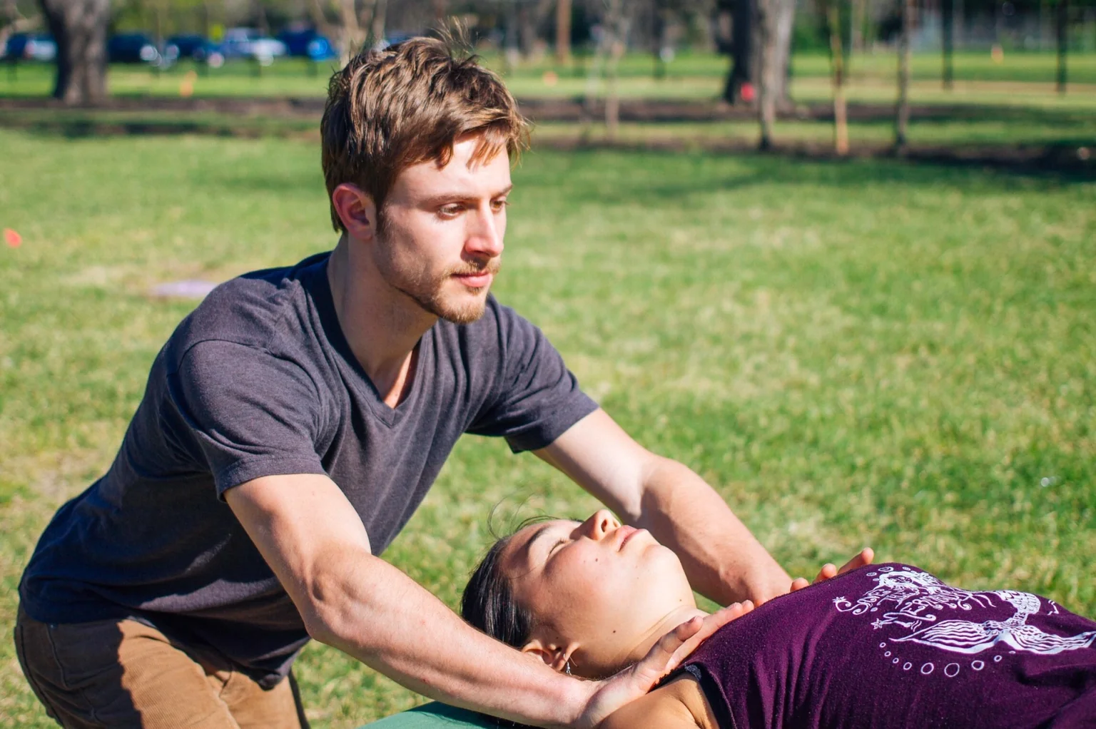 John working with a client’s neck and shoulders on a bodywork table outdoors.