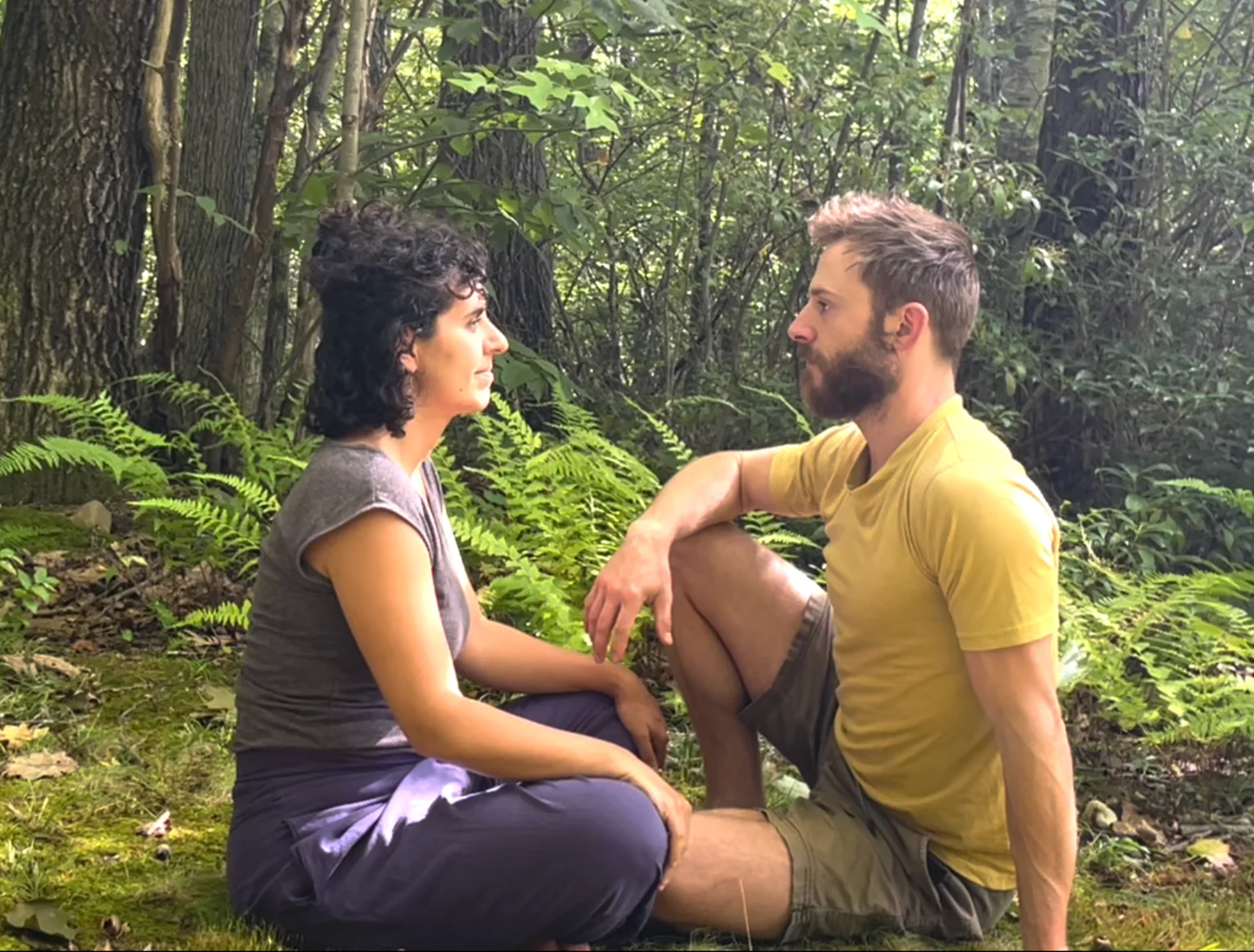 John and a partner sitting face to face in a wooded clearing.